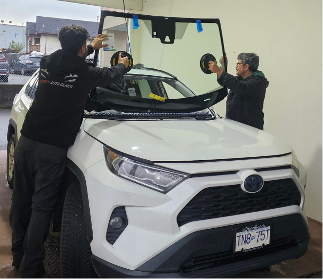Two Expert Auto Glass technicians carefully installing a new windshield on a white Toyota SUV in Surrey, BC using professional suction tools.