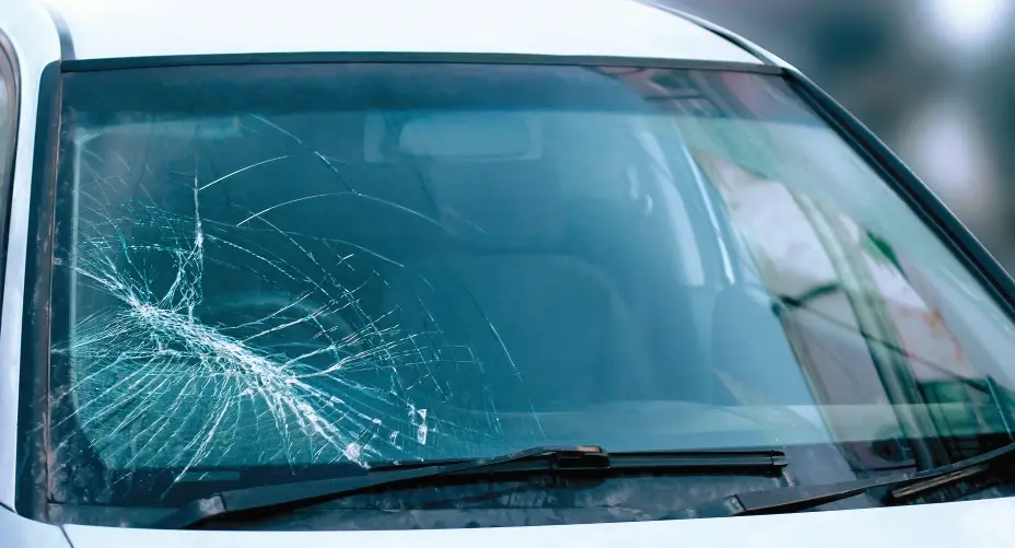 Close-up of a severely shattered and cracked front windshield on a white car requiring urgent replacement by Expert Auto Glass in Surrey.