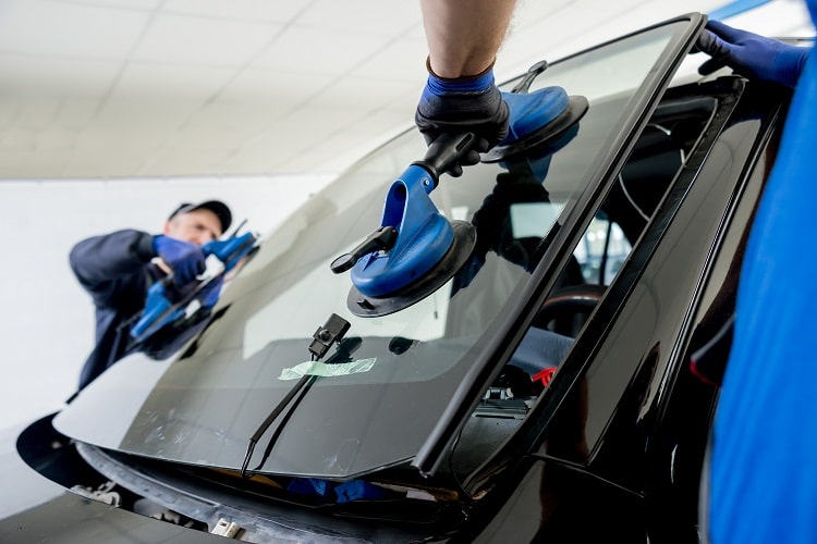 Two professional technicians from Expert Auto Glass in Surrey carefully installing a new windshield on a black vehicle using specialized suction cup tools.