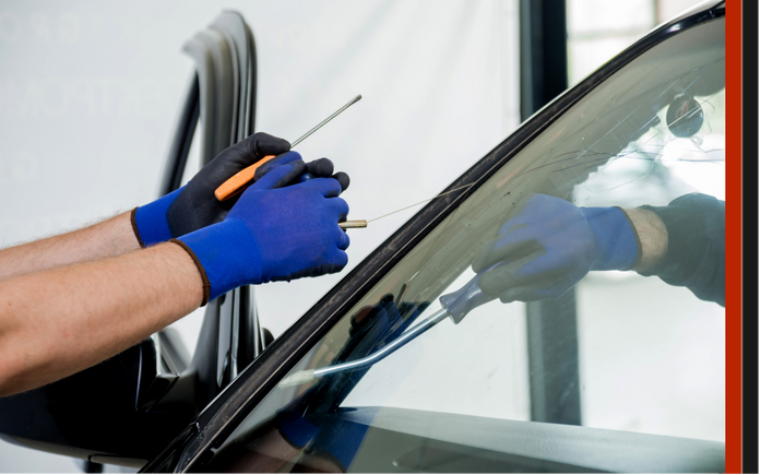 Professional technician wearing blue safety gloves using specialized tools to remove a damaged windshield for replacement in Surrey.