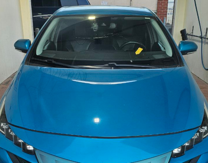 Front view of a blue car with a cracked windshield parked in a service bay, highlighting the need for auto glass repair in Surrey.