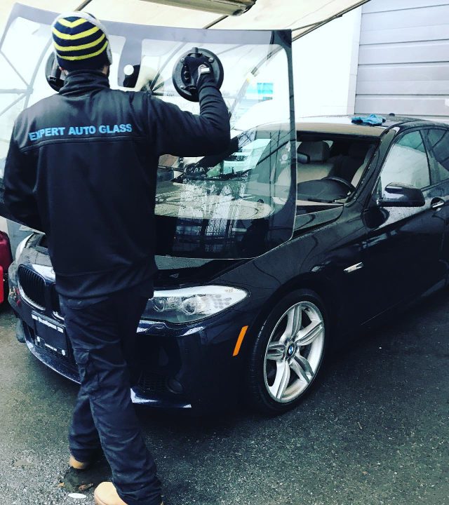 Expert Auto Glass technician installing a new windshield on a black BMW at a Surrey service location.